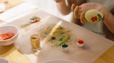 Paskalya yumurtasına kırmızı çiçek çizen bir kadın. Parlak, güneşli bir odada..