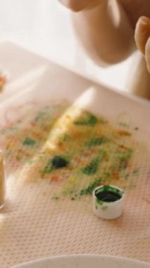 Dikey video. Paskalya yumurtasına kırmızı çiçek çizen bir kadın. Parlak, güneşli bir odada..