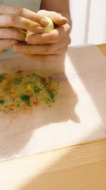 Dikey video. Paskalya yumurtasına elleri parlak, güneşli bir odada sarı renk uygulayan kadın..