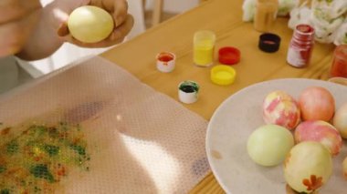 Paskalya yumurtasını parlak, güneşli bir odada yeşil noktalarla süsleyen kadın..