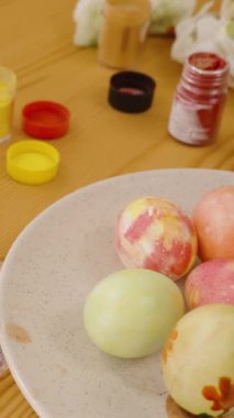 Dikey video. Paskalya yumurtasını parlak, güneşli bir odada yeşil noktalarla süsleyen kadın..