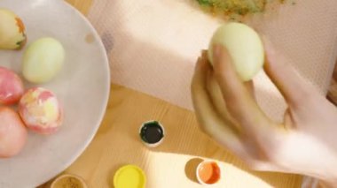 Bir el, yeşil bir Paskalya yumurtasını diğerlerinin arasına parlak, güneşli bir odada bir tabağa koyar..