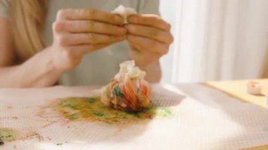 Güneşli bir odada boya kaplı bir paspasın üzerinde sarılmış bir Paskalya yumurtası yuvarlamak..