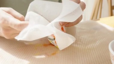 Renkli bir Paskalya yumurtasını bir bardak suya sarıp masaya bir kase boya ve boya malzemesi koyuyor..