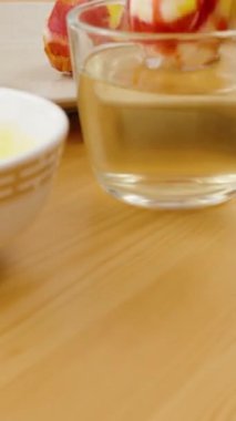 Dikey video. El, beze sarılı renkli bir Paskalya yumurtasını bir tabağa koyar. Tabağa da bir kase sarı boya ve bir bardak su koyar..