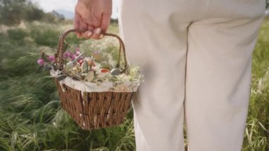 Beyaz pantolonlu bir kadın yeşil bir tarlada elinde renkli çiçekler ve paskalya yumurtalarıyla dolu bir sepet tutuyor. Yavaş çekim.