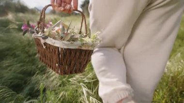 Canlı Çiçekler ve Paskalya Yumurtalarıyla Dolu Dokuma Sepeti Beyaz Pantolon Giyen Bir Kadın Tarlada Yürüyor. Yavaş çekim.