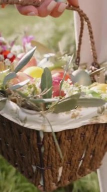 Dikey video. Çiçek ve Paskalya Yumurtası Taşıyan Bir El, Beyaz Pantolon Giyen Kadın 'ın Çimen Tarlası' nda Dolaştığı. Yavaş çekim.