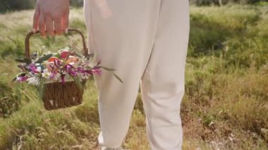 Çiçeklerle Dolu Dokuma Sepeti ve Paskalya Yumurtaları Beyaz Pantolon Giyen, Parlak Bir Tarlada Yürüyen Bir Kadın tarafından taşınır. Yavaş çekim.