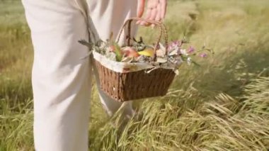 Çiçek ve Paskalya Yumurtası Sepeti Taşıyan Bir El, Beyaz Pantolon Giyen Kadın Otlakta Yürüyor. Yavaş çekim.
