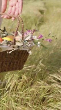 Dikey video. Çiçek ve Paskalya Yumurtası Sepeti Taşıyan Bir El, Beyaz Pantolon Giyen Kadın Otlakta Yürüyor. Yavaş çekim.