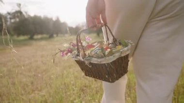 Renkli Paskalya Yumurtaları ve Çiçekleri ile dolu bir sepet tutan bir kadın tarlada yürüyor. Yavaş çekim.