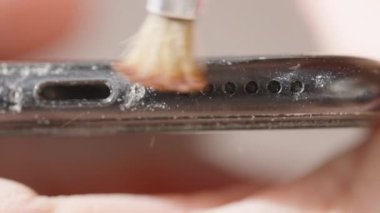 Toprağı ve parçacıkları temizlemeye odaklanmış, iyi bir fırçayla temizlenen tozlu siyah bir akıllı telefonun yakın plan görüntüsü.