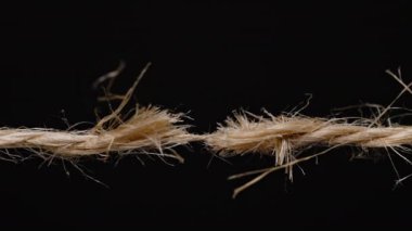Kırılmanın eşiğindeki yıpranmış bir ipin yakın çekimi, liflerdeki gerilimi ve gerilimi siyah bir arkaplanda gösteriyor. jute veya kenevir ipi