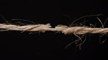 Kenevir ya da kenevir halatı. Yıpranmış bir halatın iplikleri çözünüyor. Koyu arkaplana karşı baskı altındaki gerilimi vurguluyor.