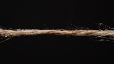 Görünür alevler ve kıvılcımlarla yanan bir halatın yakın plan çekimi. Isı altında kırılıp siyah bir arka plana doğru uzanmaya başlıyor. jute veya kenevir ipi