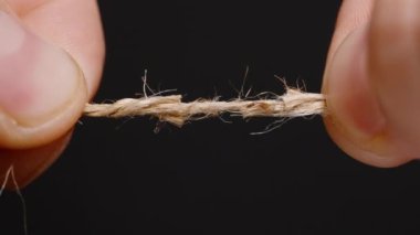 Kenevir ya da kenevir ipini ayıran iki parmağın yakın çekimi gerilimi gösterir ve lifler kopmaya başlar başlamaz çözülür.