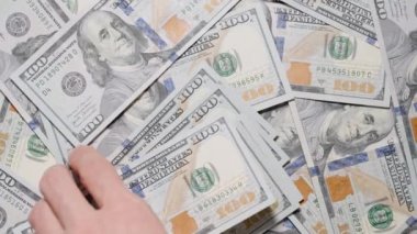 Hareket ve detaya odaklanmış bir şekilde ağır çekimde yakalanmış, dönen bir masadan 100 dolarlık banknotlar alan bir el. Işığı parayla kaplayarak.