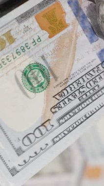 Dikey video. Bir el, yüz dolarlık banknotları, bulanık dönen dolarlarla sıkıca tutar, zenginlik ve finansal hareket kavramını yakalar.