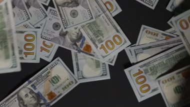 İki el bir araya gelip, yüz dolarlık banknotları karanlık bir yüzeye yığarak birikim, tasarruf ve zenginlik yönetimini sembolize ediyor.