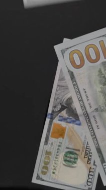 Dikey video. Yüz dolarlık banknotlar, kaotik bolluk ve finansal savurganlık göstergesi olarak bir yüzeye taşar ve dağılır.