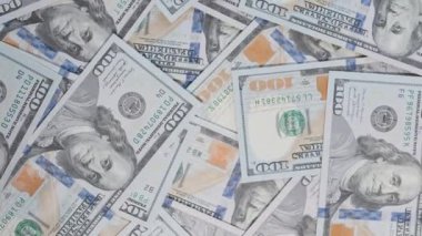 Benjamin Franklin 'in portresi ve görünür parasal sembollerinin detaylı özellikleriyle dağınık yüz dolarlık banknotların hava görüntüsü dönen bir hareketle çekildi.
