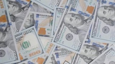 Dağınık yüz dolarlık banknotların hava görüntüsü, döndüklerinde düzenlemelerini ve hareketlerini gösteriyor, finansal akışı ve parasal bolluğu vurguluyorlar.
