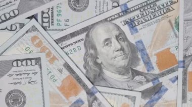 Yukarıdan izlenen dağınık yüz dolarlık banknotların yakın plan çekimleri, para biriminin karmaşık detaylarını vurgulamak için dönen bir hareketle çekildi.