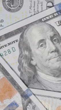 Dikey video. Yukarıdan izlenen dağınık yüz dolarlık banknotların yakın plan çekimleri, para biriminin karmaşık detaylarını vurgulamak için dönen bir hareketle çekildi.