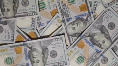 100 dolarlık banknotların üzerinde pürüzsüz bir şekilde süzülen yakın çekim görüntüsü notların tasarımı ve dokusunun karmaşık detaylarını yakalıyor.