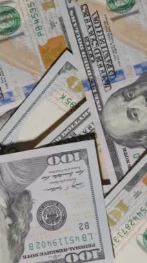 Dikey video. 100 dolarlık banknotların üzerinde pürüzsüz bir şekilde süzülen yakın çekim görüntüsü notların tasarımı ve dokusunun karmaşık detaylarını yakalıyor.