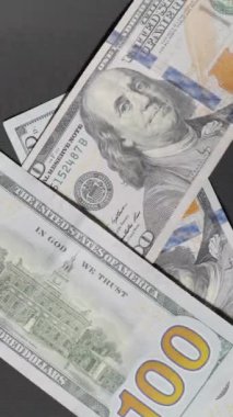 Dikey video. Yüz dolarlık banknotlar çağlayarak aşağı iniyor, yüzeyi tamamen dinamik bir nakit akışıyla kaplıyor, finansal bolluk ve refah ortamı yaratıyor.