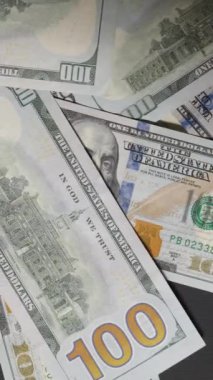 Dikey video. Bir el açgözlülükle masadan yüz dolarlık banknotları toplar, onları hızlı bir hareketle süpürür, hırsı, açgözlülüğü ya da finansal hakimiyeti sembolize eder,