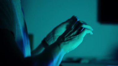 Bir kadın, tırnaklarını yumuşak mavi ışığın altında inceliyor, sakin ve içe dönük bir atmosfer yaratıyor ve ellerine odaklanıyor.