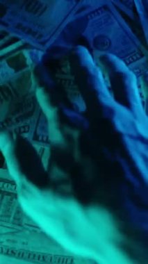 Dikey video. Bir elin hüzünlü mavi ışıklandırma altında bir yığın Amerikan doları banknotunu araması, gizem ve entrika hissi yaratıyor.