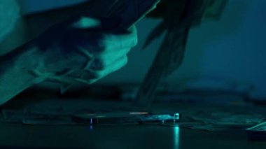 Bir kadın, yumuşak mavi ışığın altında Amerikan doları banknotlarını düzenli bir şekilde düzenliyor, elleri masanın üzerindeki notları dikkatlice düzenliyor.