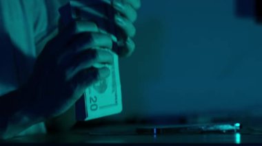 Huysuz mavi ışıklandırmanın altındaki bir masaya Amerikan doları banknotlarını istifleyerek ve düzenleyerek finansal organizasyon ve kontrol üzerine odaklanan bir kadının ellerine yakın çekim