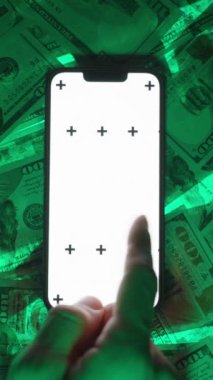 Dikey video. Beyaz Ekran Modelleri ve İzleme İşaretleri ile Smartphone 'un Üstten Görünümü, ABD Yüz Dolarlık Faturalar, Dijital Etkileşimi Depolama ve Çevrimiçi Ticaretin Yeşil Parlak Arkaplanı Üzerinde Konumlandırılmış