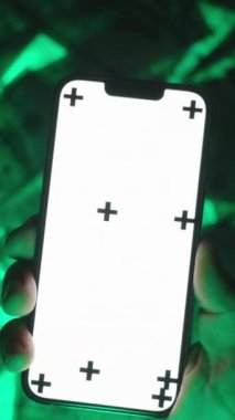 Dikey video. Boş Beyaz Ekran Modelleri ve İzleme İşaretleri ile akıllı telefondaki resmi en aza indirmek için Çimdik Hareketi Yapan Ellerin Kapanışı, ABD Yüz Dolarlık Tasarrufların Yeşil-Parlak Arkaplanı Üzerinde Konumlandırıldı