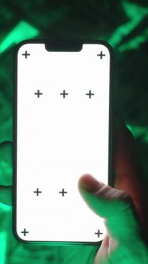 Dikey video. Boş Beyaz Ekran Modelleri ve İzleme İşaretleri ile Smartphone 'da Swipe-Left Hareketi Yapan Bir Elin Yakın Çekimi, ABD Yüz Dolarlık Faturaların Yeşil Parlak Arkaplanı Üzerinde Konumlandırılmış, İnternet Ticareti Temsilcisi