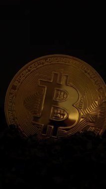 Dikey video. Bitcoin madeni parası karanlık kayalardan sarkan, Aydınlığın parlak yüzeyinden yansımasıyla yavaşça karanlıktan ortaya çıkan. Dijital Altın ve Madencilik Konseptini temsil eder