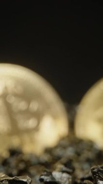 Dikey video. İki Bitcoin madeni para yavaş yavaş Karanlık, desenli kayaların üzerinde dinlenirken odak noktasına geliyor. Onların parlak yüzeyleri ışığı yansıtır, netliği ve dijital zenginliği sembolize eder.