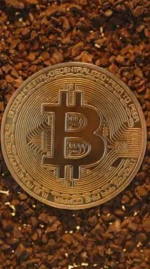 Dikey video. Dijital varlıkların dünyevi materyallerle karışımını ve Madencilik kavramını temsil eden küçük çakıl taşlarının üzerine uzanan bir Bitcoin madeni para.