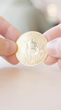 Dikey video. Yakından Bakış Açısı 'ndan Yumuşak Arkaplan Görüntü ile Tahta Yüzey' de Altın Bitcoin Madeni Para Tutan İki El. Şifreleme ve Dijital Aktarımlar Konsepti