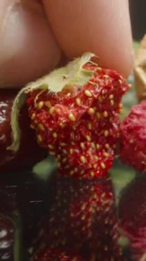 Dikey video. Yansıtıcı yüzeyde kurutulmuş kivi ve ahududu yanında görülebilir tohumlu kurutulmuş çilek tutuyorum. Doku ve meyve çürümesine odaklan