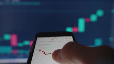 El Tutma Akıllı Telefonu Bitcoin Çizelgesi Candlesticks, Arkaplan Bulanık Kripto Para Birimi Verisi ve Bilgisayar Ekranında Grafikler, Düşük Açı Görünümü