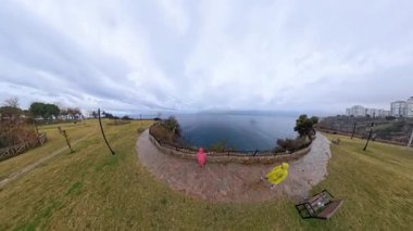 Bulutlu bir günde Engin Deniz 'e bakan, Çit ve Kıyı Bitkisi Tarafından Çerçevelenen Taş Bir Yolda Duran Yağmurluklu Bir Çift