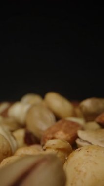 Dikey video. Karanlık Bir Arkaplana Karşı Yavaş Çekimde Düşen Karışık Fındıkların Yakın Çekim Görünümü Hareketi ve Dokusunu Vurguluyor. Sağlıklı atıştırmalıklar veya organik gıdalar