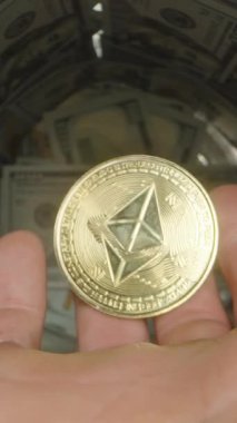 Dikey video. Yüz Dolarlık banknotlarla dolu bir kavanoza altın bir madeni para düşüren, Harmanlama Varlıklarının Hareket ve Sembolizmini yakalayan Bir El 'in Yakın Çekim Görüntüsü