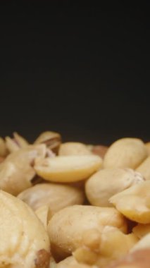 Dikey video. Kaypak Hareketli Karışık Ceviz Yığını Karanlık Bir Arkaplana Karşı Yakından Bakış, Doku ve Doğal Renkleri Vurguluyor. Konsept: Besleyici Gıda veya Atıştırma Çeşitliliği